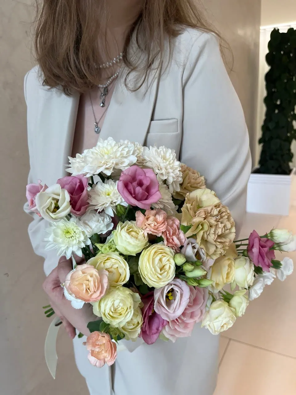A woman at a white wall holding a pastel bouquet of roses and lisianthus