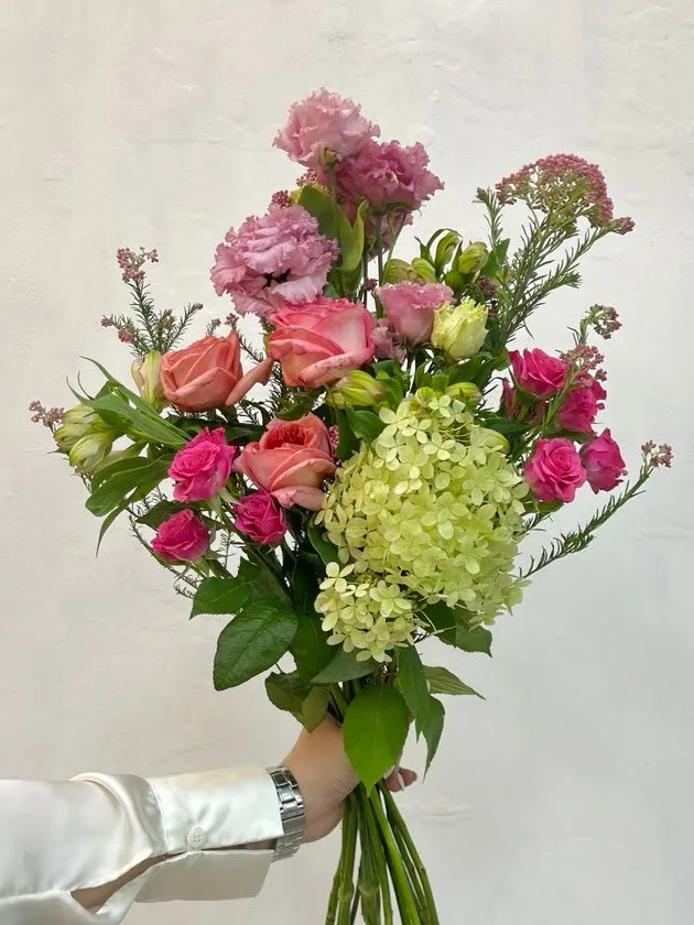 Ramo de hortensia, rosas y lisianthus extendido frente a una pared blanca