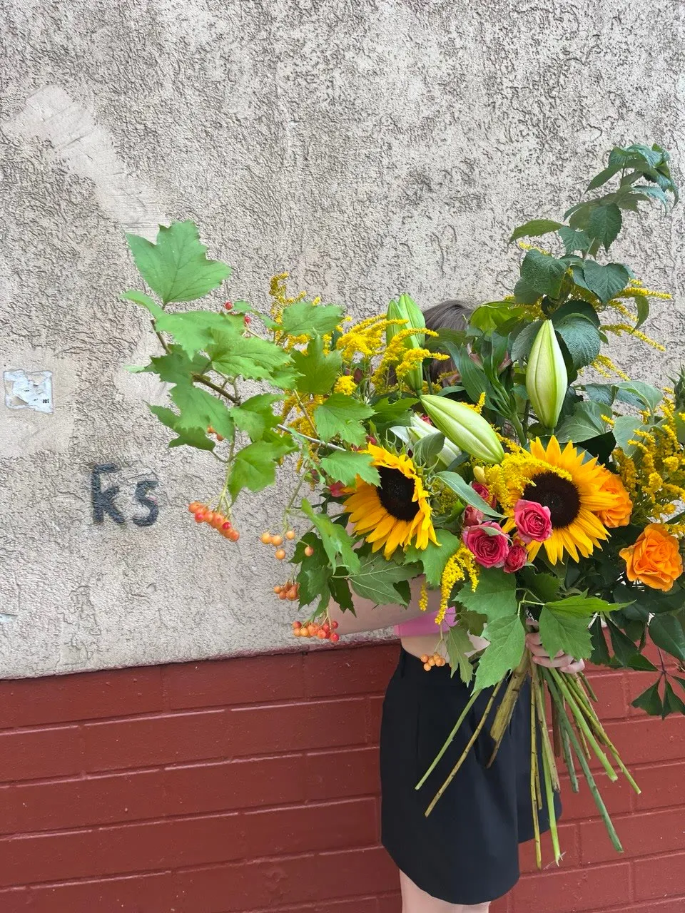Gran ramo de girasoles, lirios, solidago y viburno junto a una pared