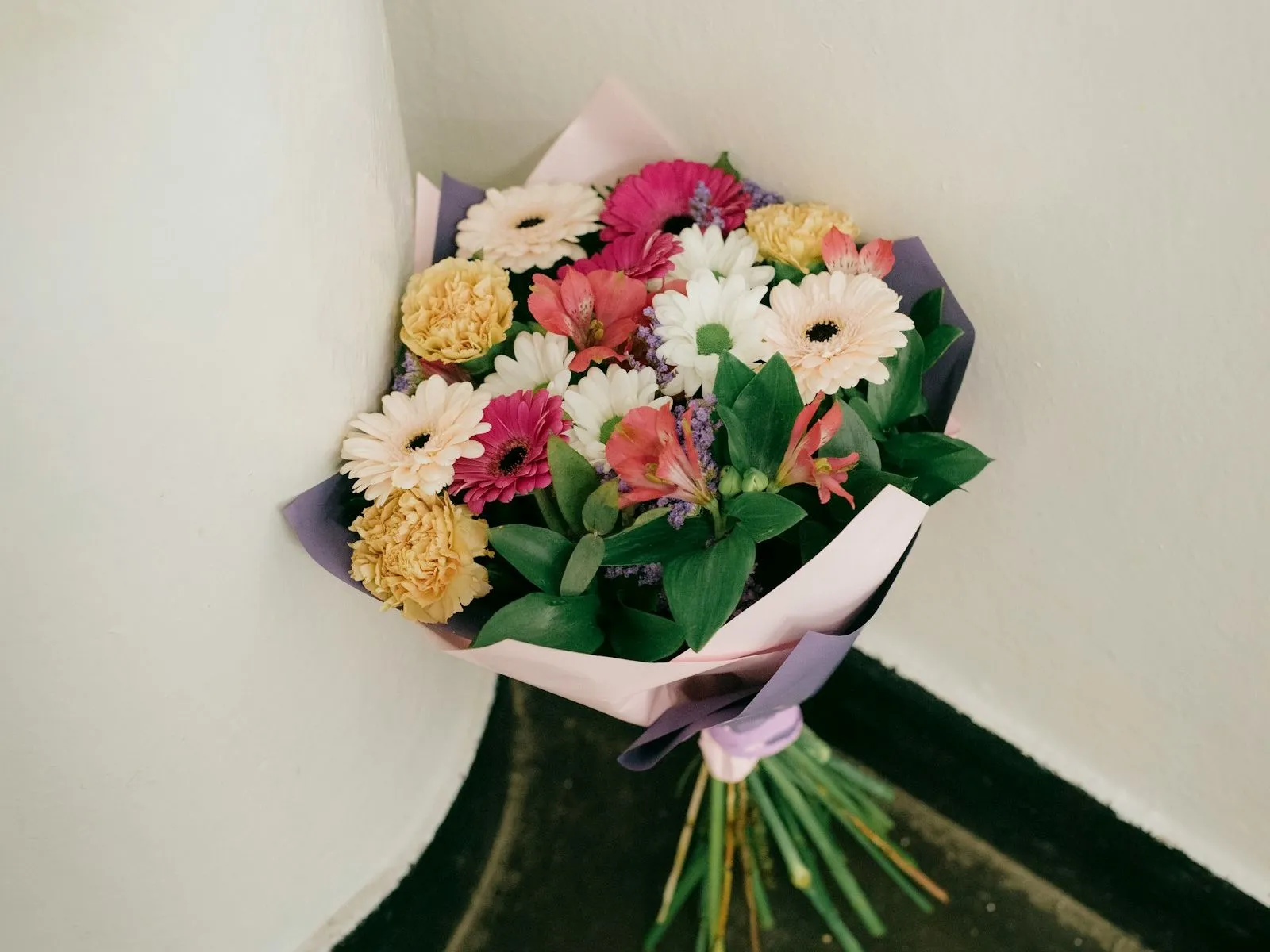 Ramo de gerberas, claveles, margaritas y astromelias envuelto en papel rosado y violeta