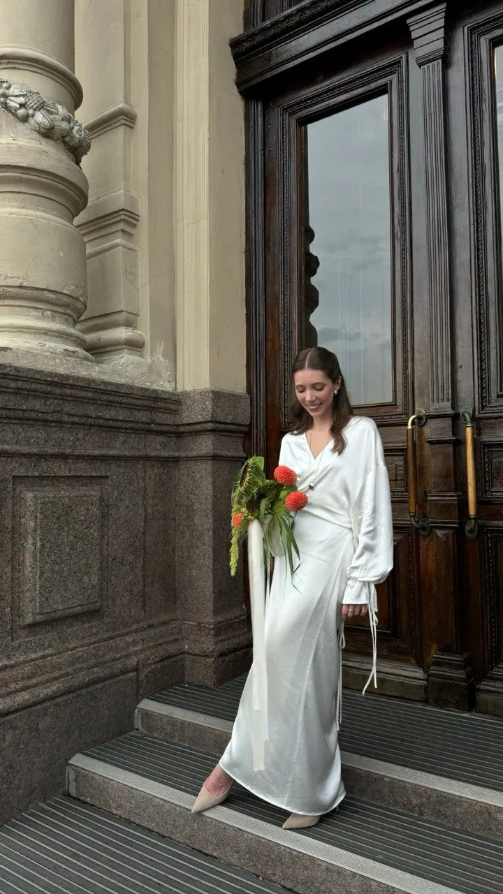 A bride in a white silk dress holding a bouquet of orange blooms and foliage